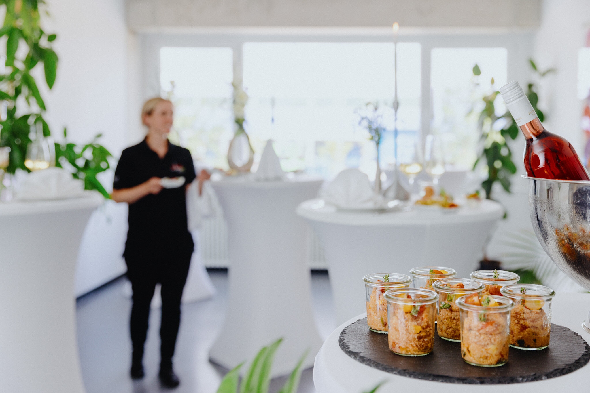 Eingedeckte Hochtische im Raum verteilt und auf dem vorderen Tisch stehen Fingerfoord Häppchen