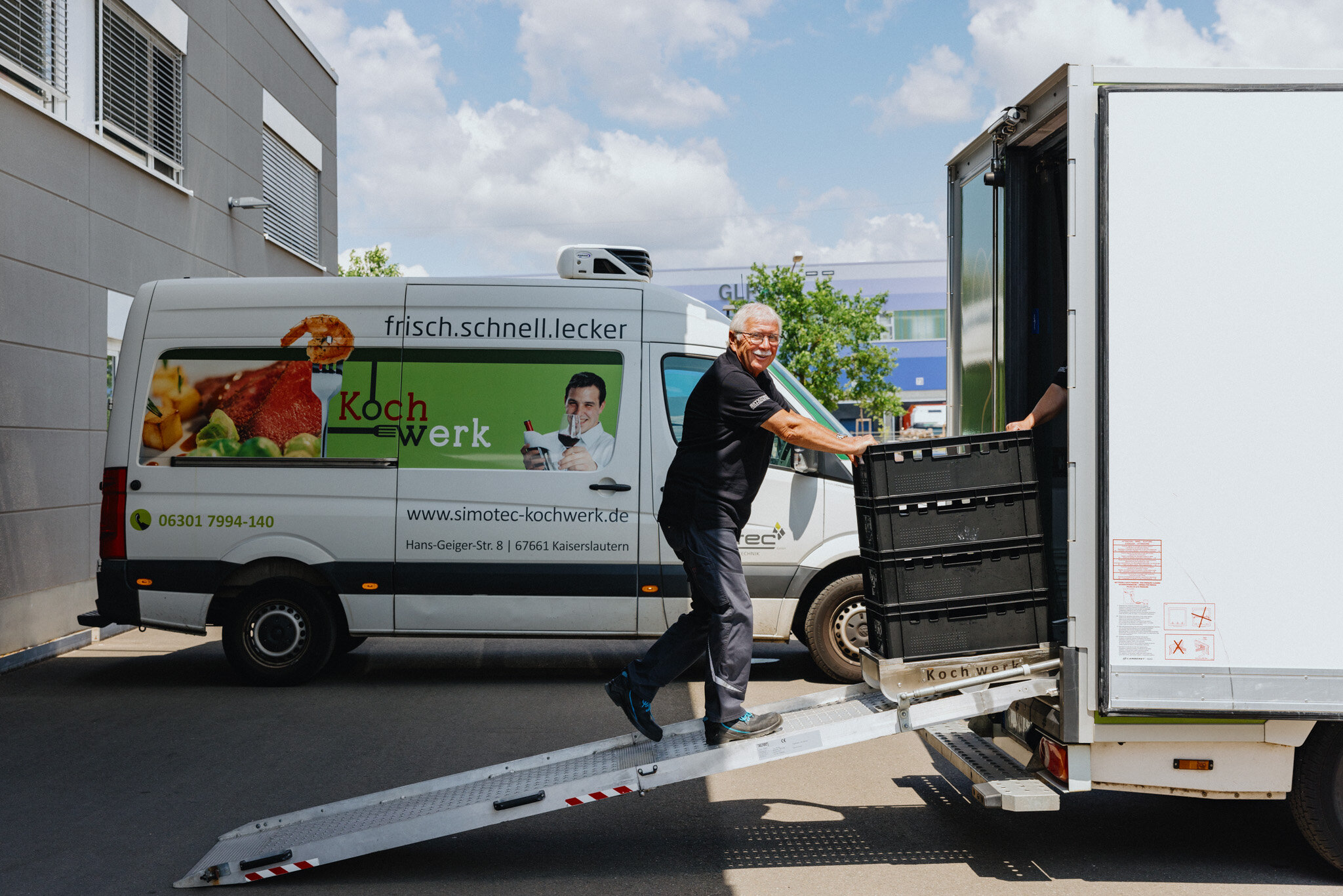 Ein Mann schiebt Kisten eine Rampe am Fahrzeug hoch